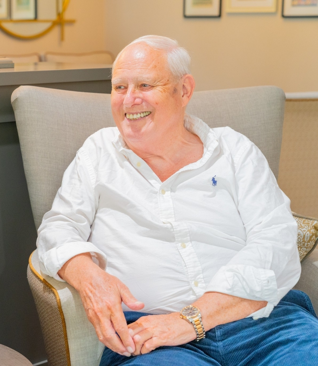 A male resident wearing a white shirt and jeans smiling in a comfortable armchair